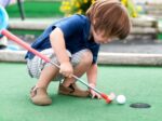 little kid playing mini golf